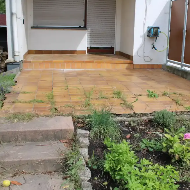 Alte Terrasse mit Unkraut und Gras in den Fugen vor der Sanierung mit einer fugenlosen Marmorstein-Beschichtung in Südbaden.