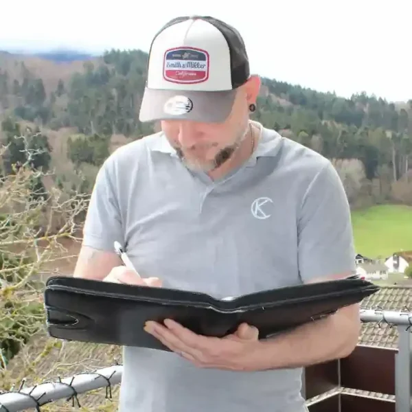 Stefan Ketterer plant ein Projekt mit dem Auftragsbuch in der Hand, um Notizen für eine Balkonsanierung zu machen.
